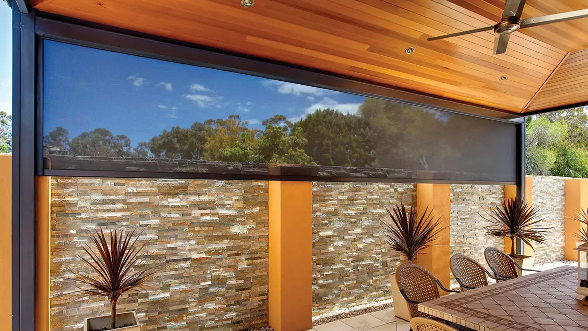 High-quality dark mesh outdoor motorized track blind installed on a luxury patio with a wooden ceiling, providing sun shade and wind protection for outdoor living areas.